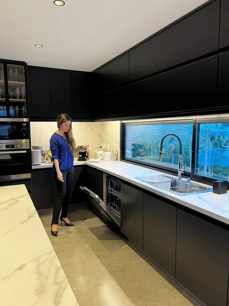 Cocina negra en L con lavavajillas integrado y ventana larga sobre la mesada